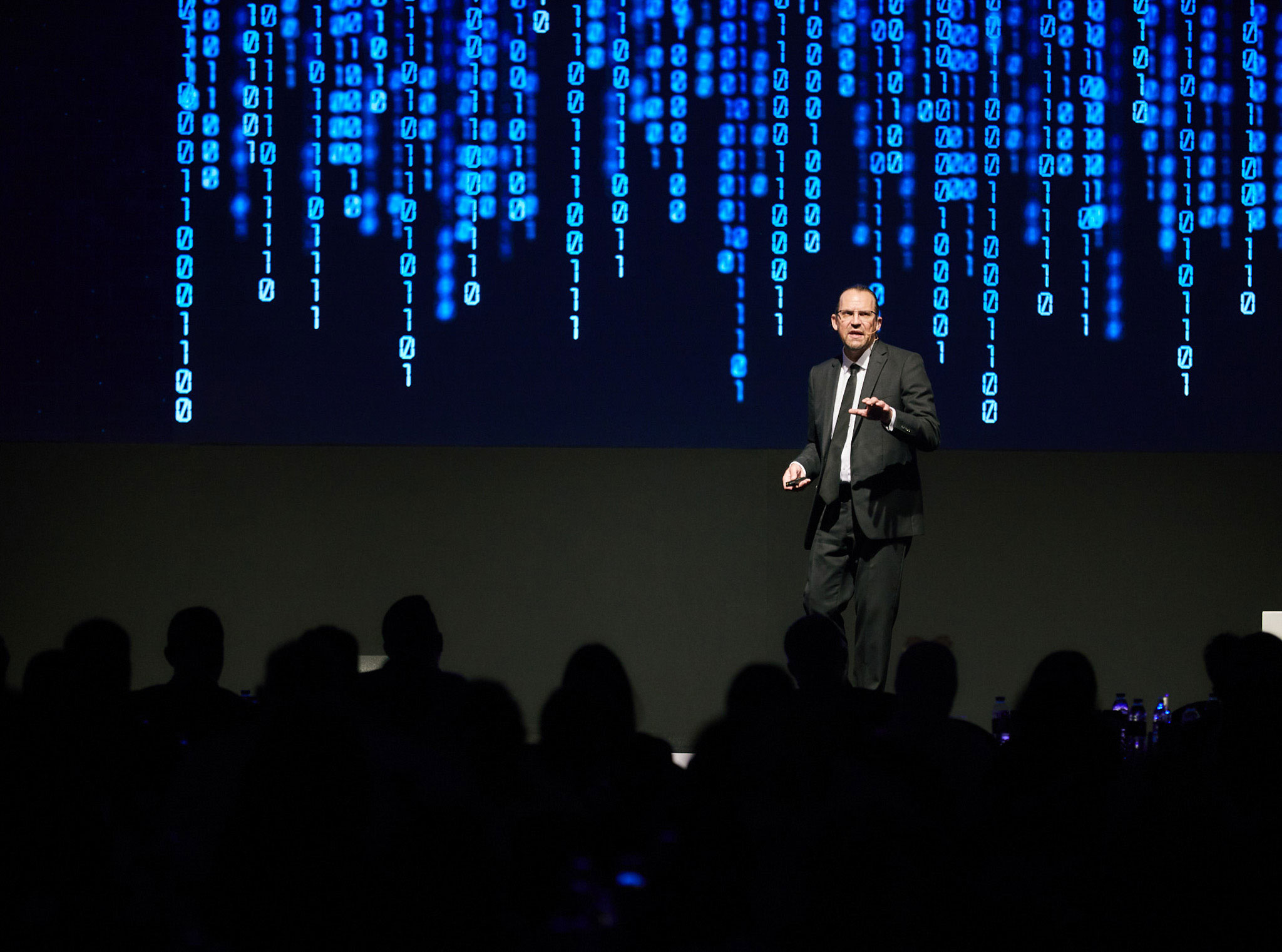 Dave Coplin presenting on stage with a digital binary code backdrop
